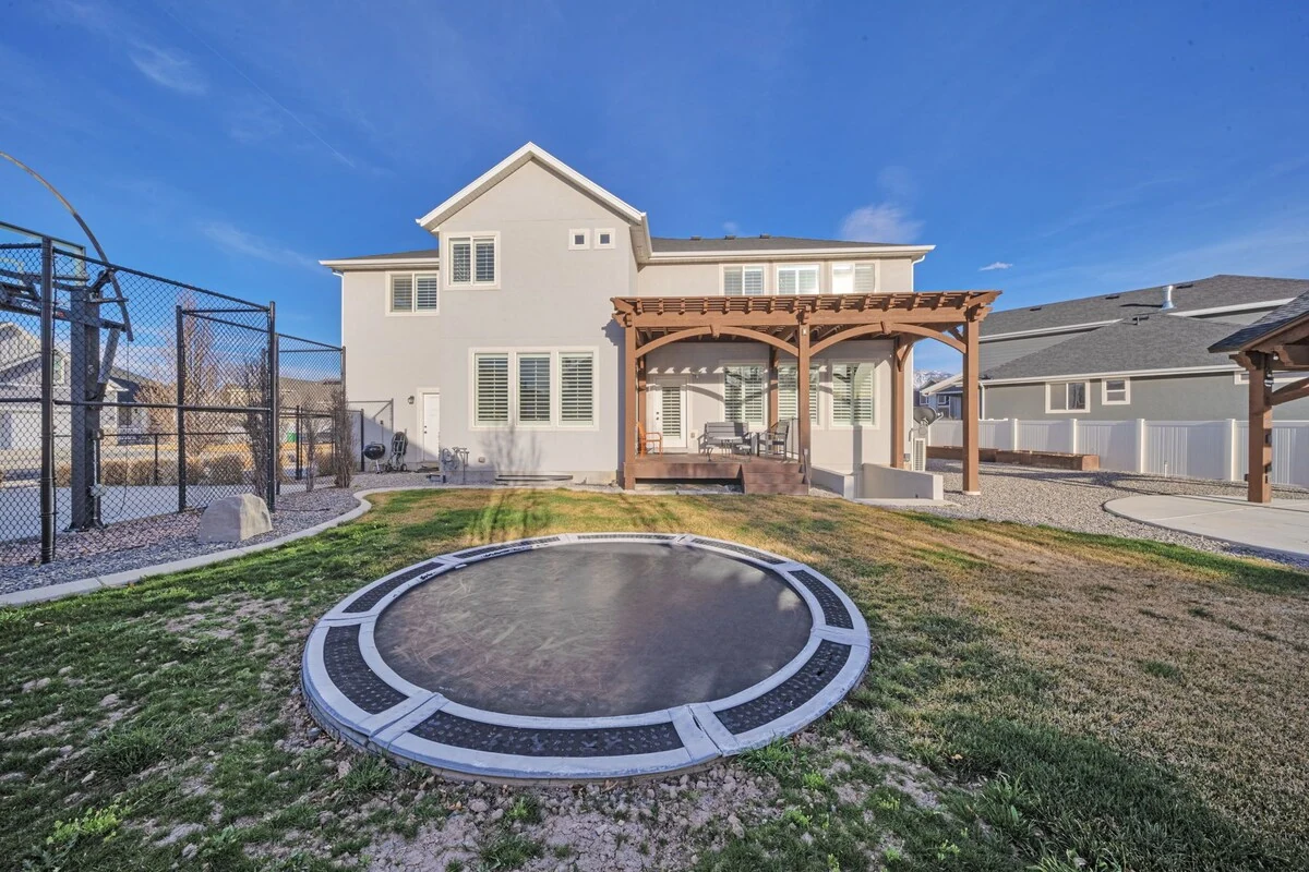 Backyard with an in-ground trampoline, lawn, and pergola-covered deck